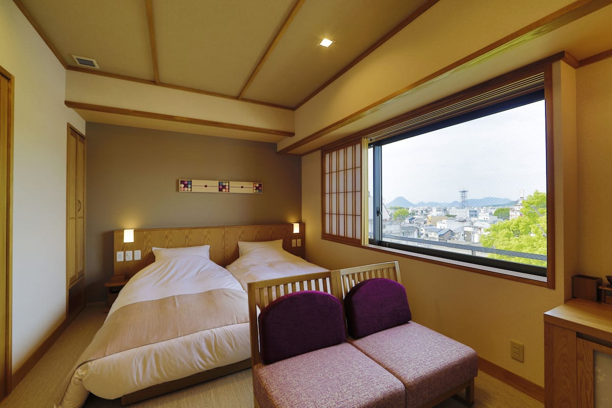 Une chambre d’hôtel avec deux lits, un petit coin salon et une fenêtre donnant sur la ville.