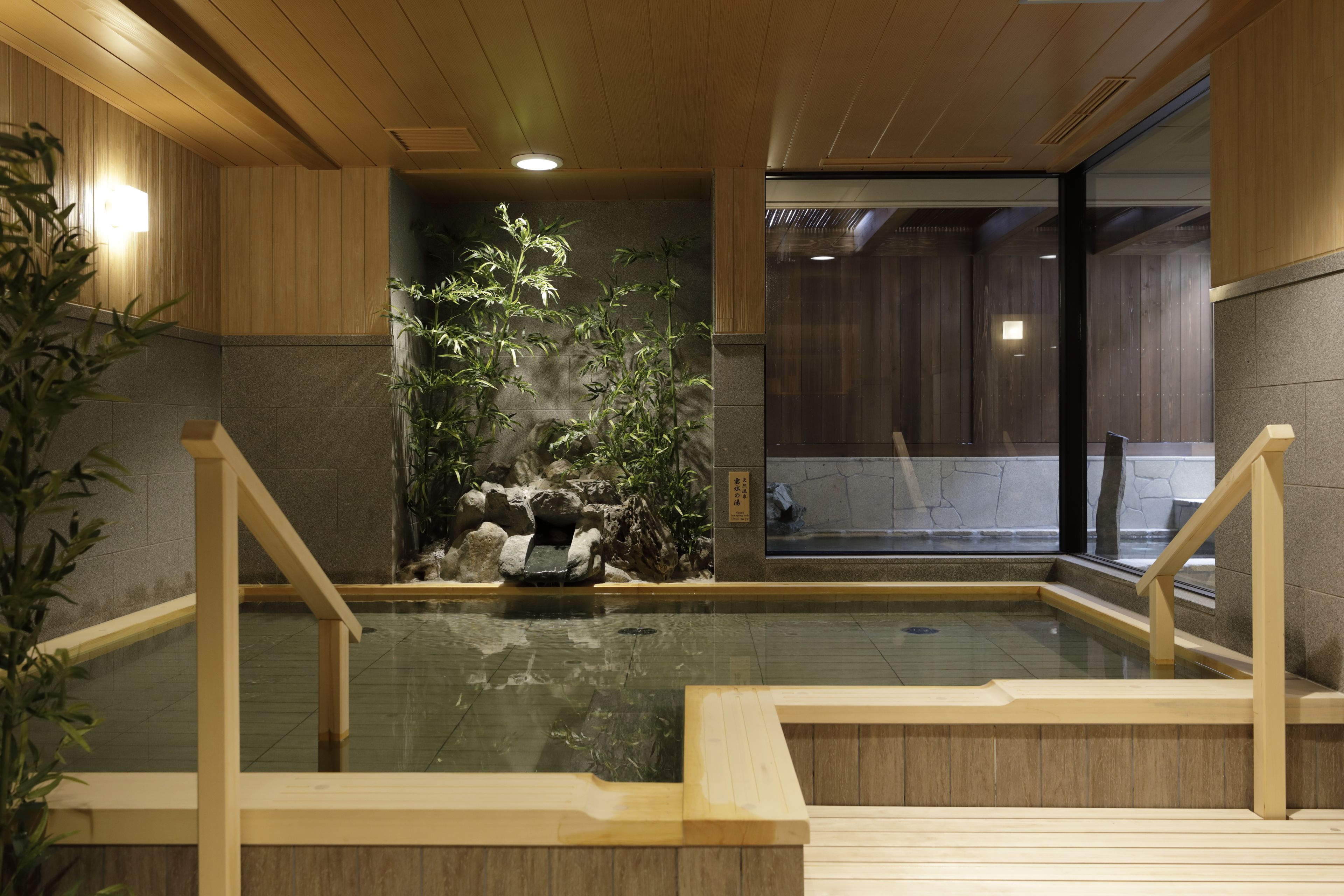A traditional Japanese onsen with wooden railings, a rock garden, and a view of the outside.