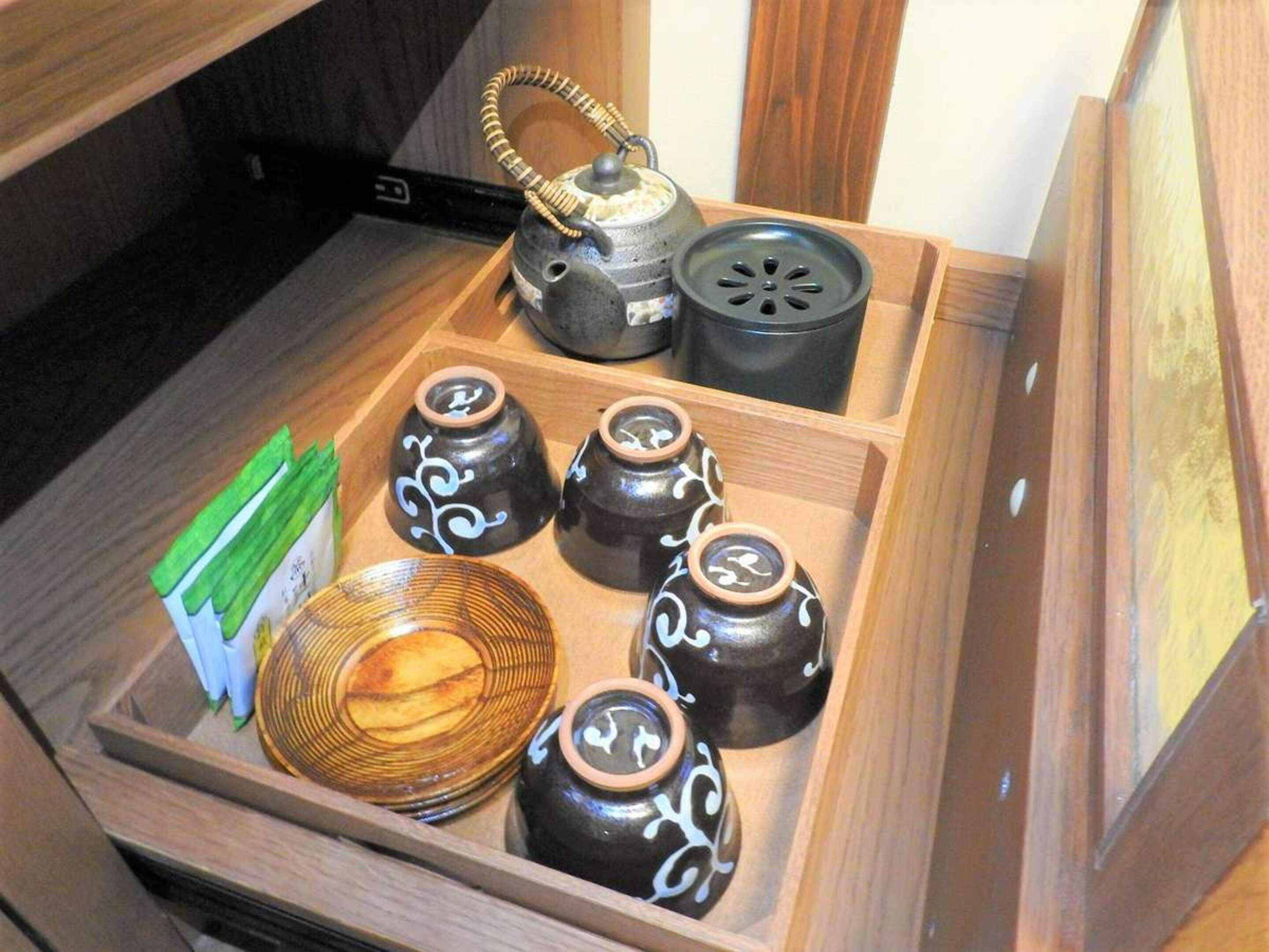 Uma gaveta de madeira com diversos utensílios de cozinha, incluindo um bule, uma panela elétrica e vários pequenos vasos de cerâmica com desenhos decorativos.