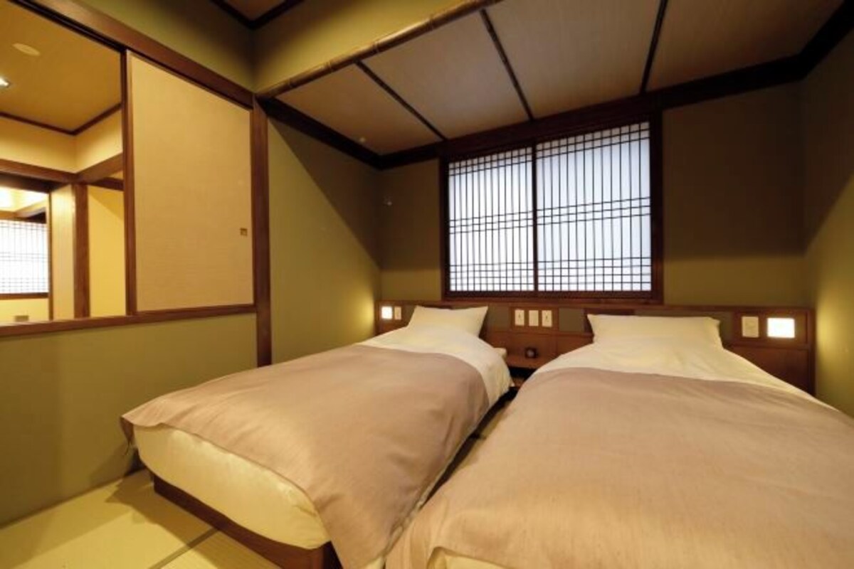 A traditional Japanese-style room with two beds, wooden headboards, and a shoji screen window.