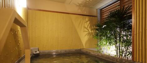 A hot spring area with a stone pool, bamboo walls, and a wooden staircase.
