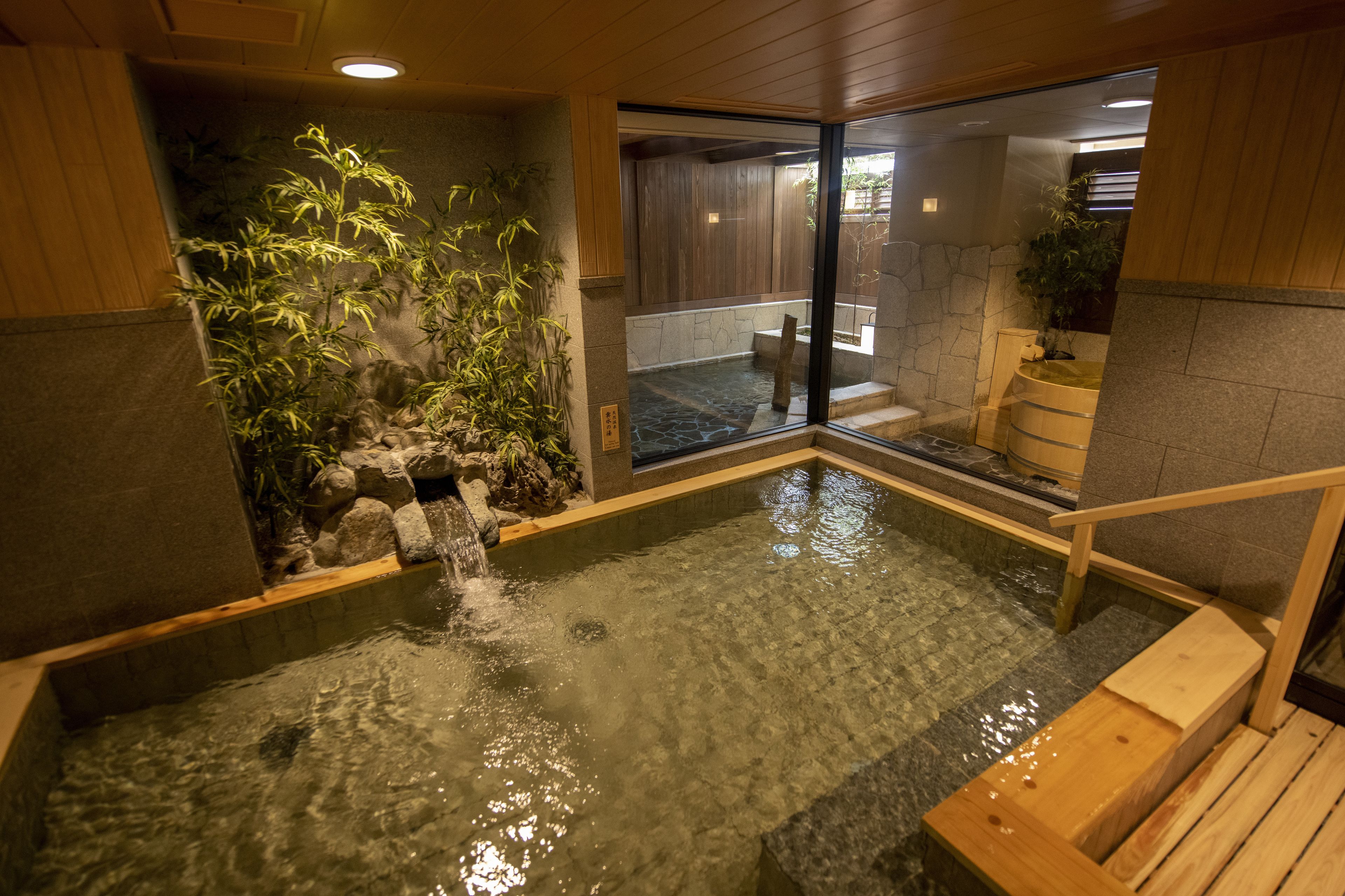 Un baño de aguas termales con una terraza de madera y un muro de piedra.