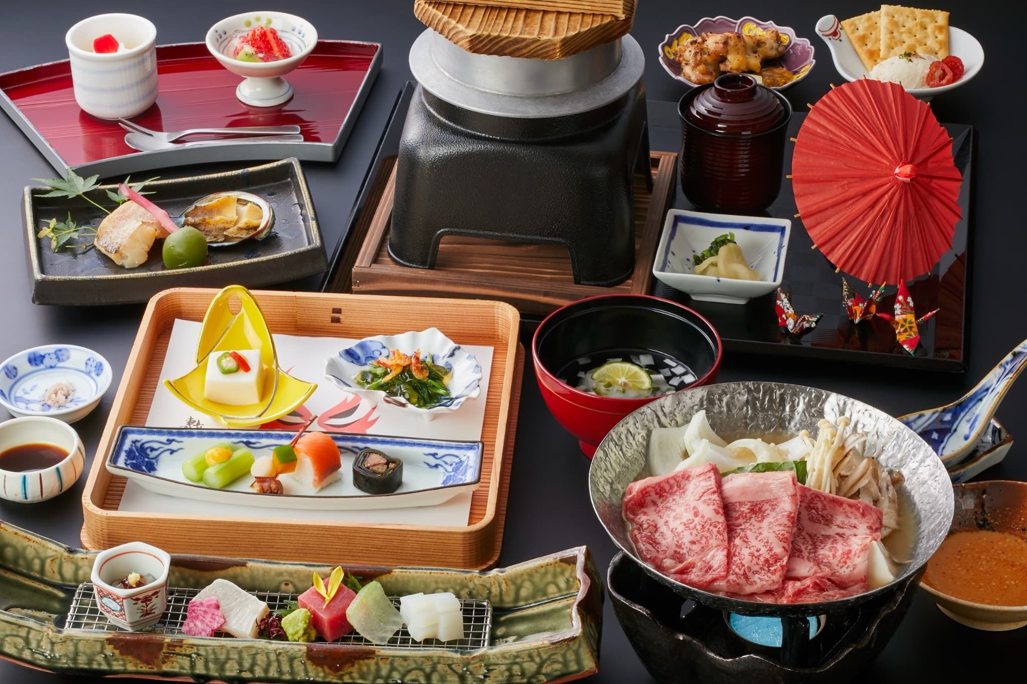 A variety of Japanese dishes and utensils on a table, including sushi, sashimi, and a hot pot.