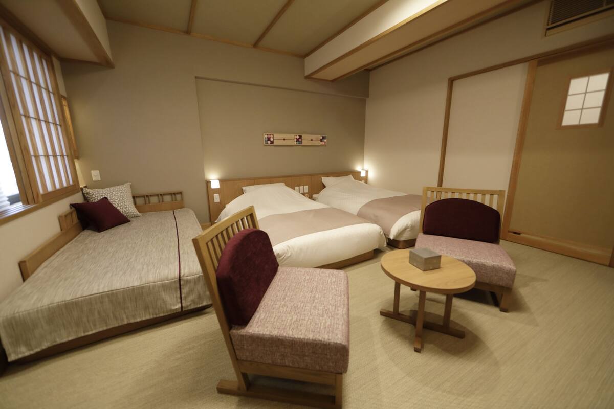 Une pièce de style japonais traditionnel, avec un sol recouvert de tatamis, un lit bas en bois, un fauteuil rembourré, une petite table ronde et une porte coulissante.