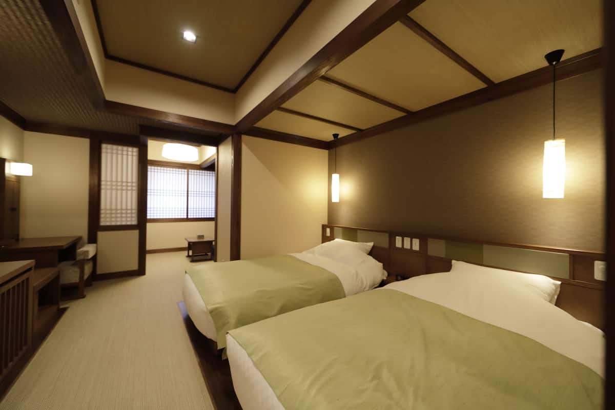 Une chambre d’hôtel avec deux lits, des têtes de lit en bois et un paravent japonais traditionnel en papier.