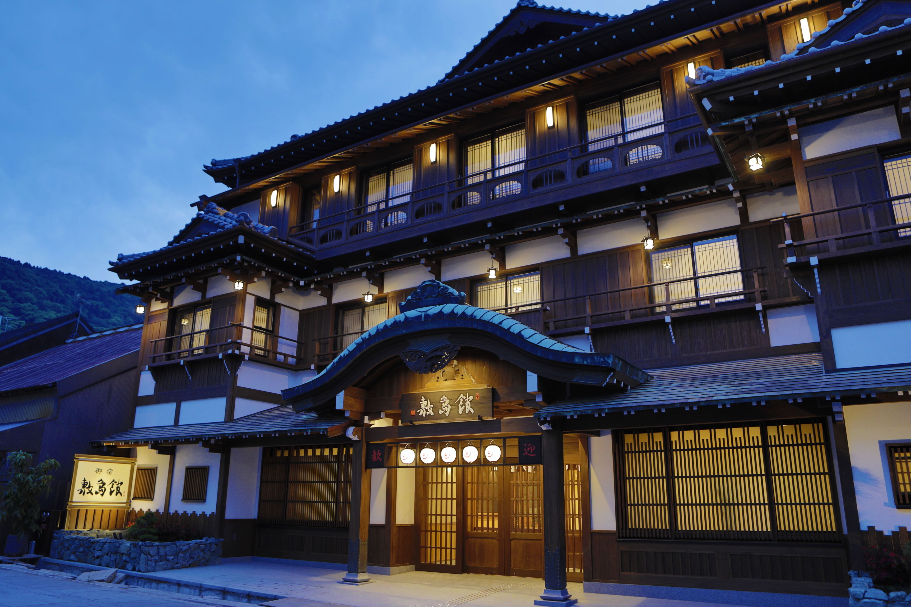 Un edificio japonés tradicional de varios pisos, con balcones de madera y un letrero que indica que es un ryokan.