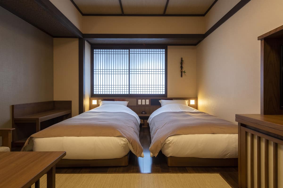 Une pièce de style japonais traditionnel, avec deux lits simples, un banc en bois et une grande fenêtre à carreaux.