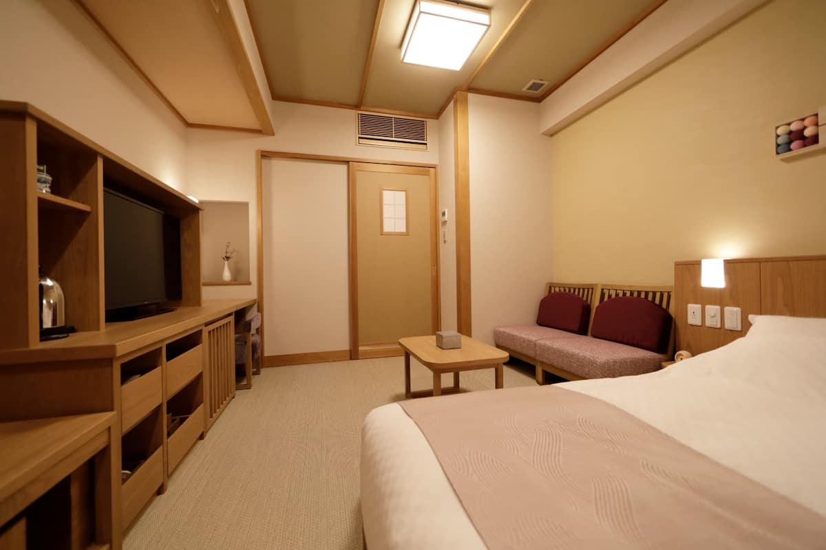 Une chambre d’hôtel avec un lit, un téléviseur posé sur un meuble en bois, une petite table, un canapé et une armoire.