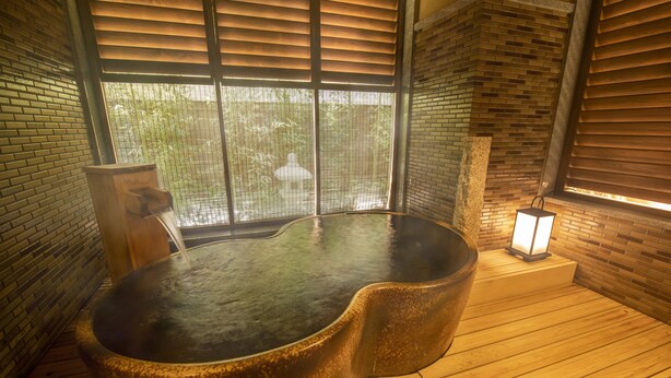 Ein Whirlpool in einem Zimmer mit Holzboden und Backsteinwänden, ein Fenster mit Jalousien und ein kleiner Tisch mit Lampe.
