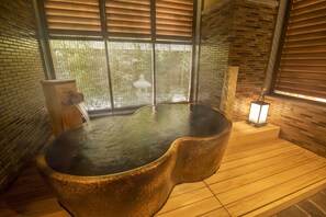 Ein Whirlpool in einem Zimmer mit Holzboden und Backsteinwänden, ein Fenster mit Jalousien und ein kleiner Tisch mit Lampe.