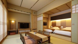 Ein traditioneller japanischer Raum mit Tatami-Boden, einem niedrigen Holztisch, zwei Betten und einem Fernseher.