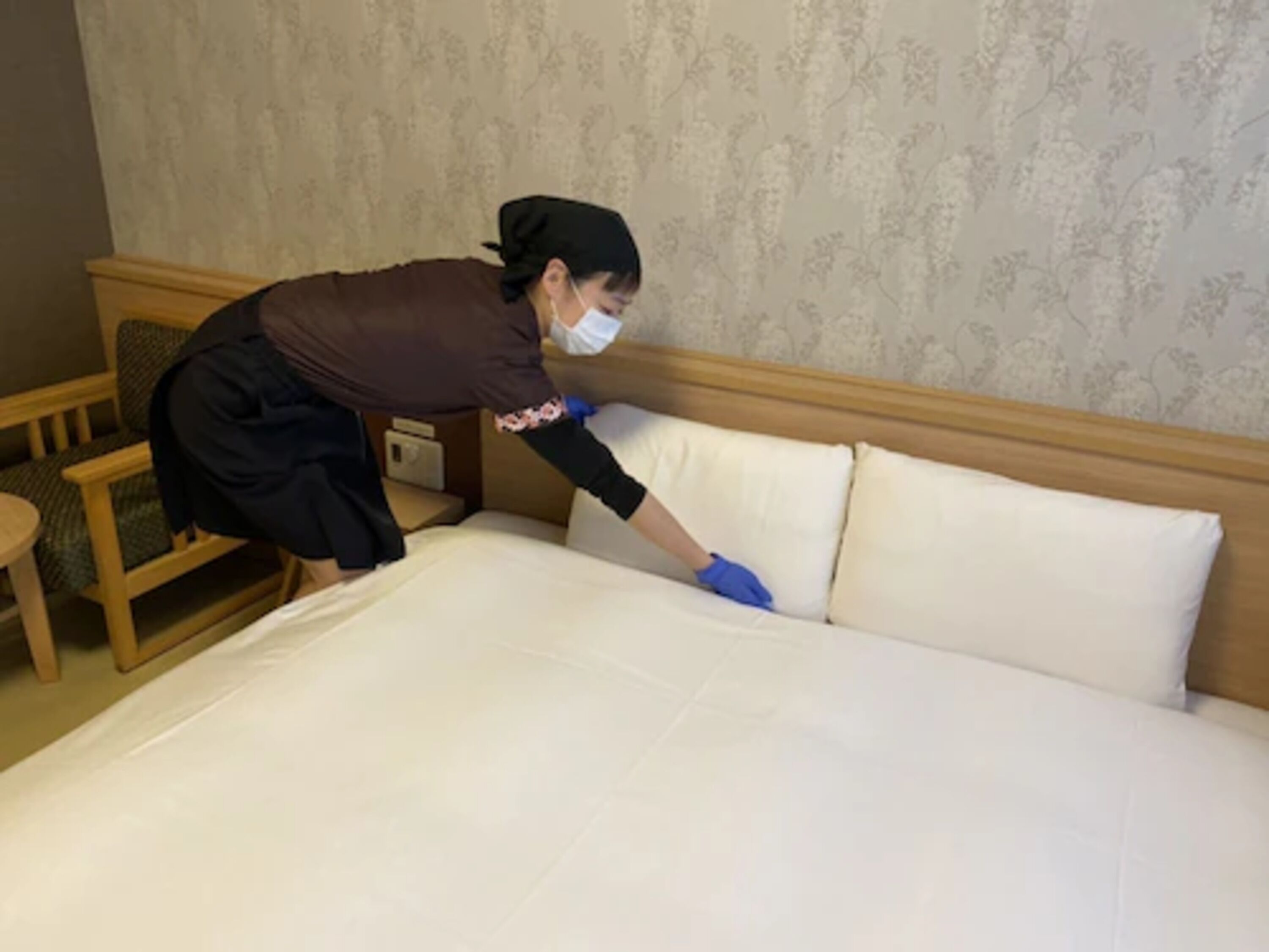 A hotel room with a neatly made bed, a wooden headboard, and a floral wallpaper pattern.