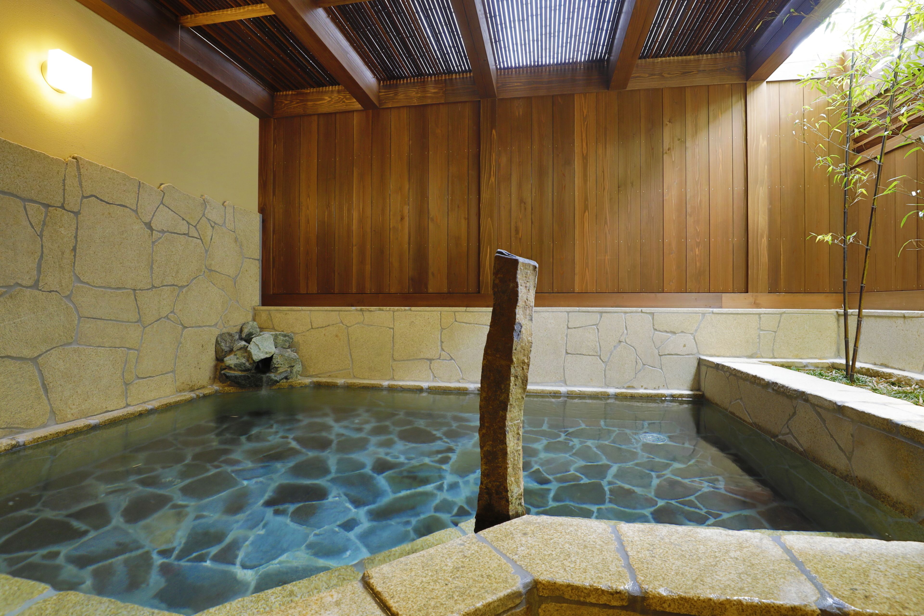 A stone-lined hot spring with wooden walls and a tiled ceiling.