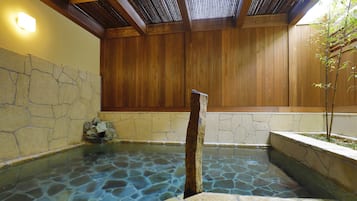 A stone-lined hot spring with wooden walls and a tiled ceiling.