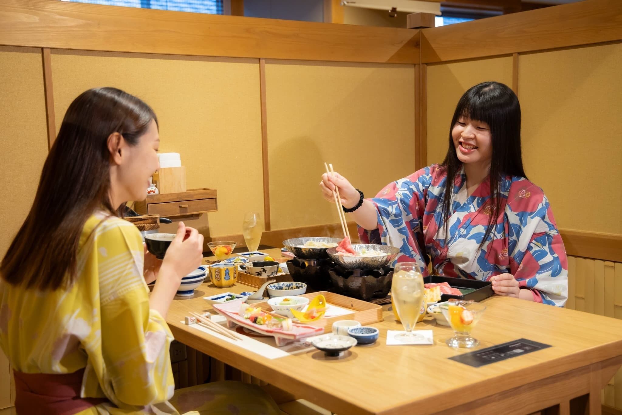 Two people dining at a table with various dishes, chopsticks, and a teapot.