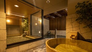 Ein traditionelles japanisches Onsen mit einer Holzwanne, Steinwänden und einer Bambuspflanze.