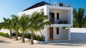 A modern two-story building with a flat roof, a balcony on the upper floor, and a gravel driveway. - Sugar Kube Villa Turks & Caicos – Romantic 1BR Villa with Private Pool & Rooftop Deck (Grace Bay)