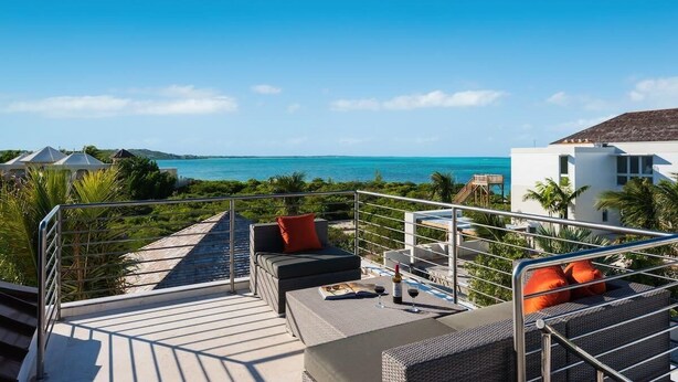 A rooftop terrace with a view of the ocean, outdoor seating, and a staircase leading to the upper level. - Sugar Kube Villa Turks & Caicos – Romantic 1BR Villa with Private Pool & Rooftop Deck (Grace Bay)