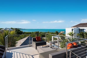 A rooftop terrace with a view of the ocean, outdoor seating, and a staircase leading to the upper level. - Sugar Kube Villa Turks & Caicos – Romantic 1BR Villa with Private Pool & Rooftop Deck (Grace Bay)