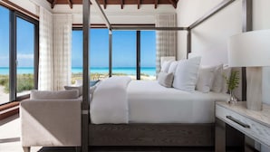 Quarto com uma cama grande, mesa de cabeceira, cadeira e vista para a praia.