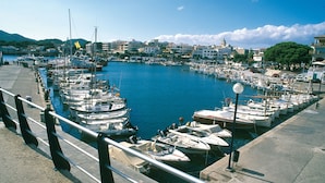 A marina with numerous boats docked, a clear sky, and buildings in the background. - Apartment Can Serol 2 (Capdepera)