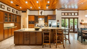 Una cocina amplia con armarios de madera, una isla grande con taburetes de bar y vistas al exterior a través de las ventanas.