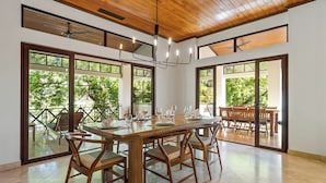 Un vaste espace dédié à la salle à manger, avec une table et des chaises en bois, de grandes fenêtres offrant une vue sur la verdure et un lustre moderne.