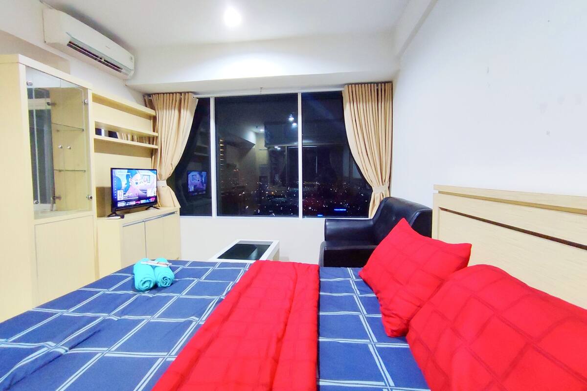 A hotel room with a bed, a chair, a TV, and a window with a city view.