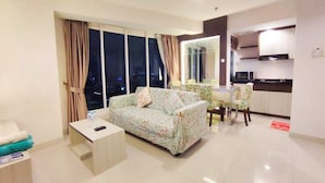 A modern living room with a sofa, a small table, and a dining area with a table and chairs. - Grand Kamala Lagoon By Mitra Propertindo (Bekasi)