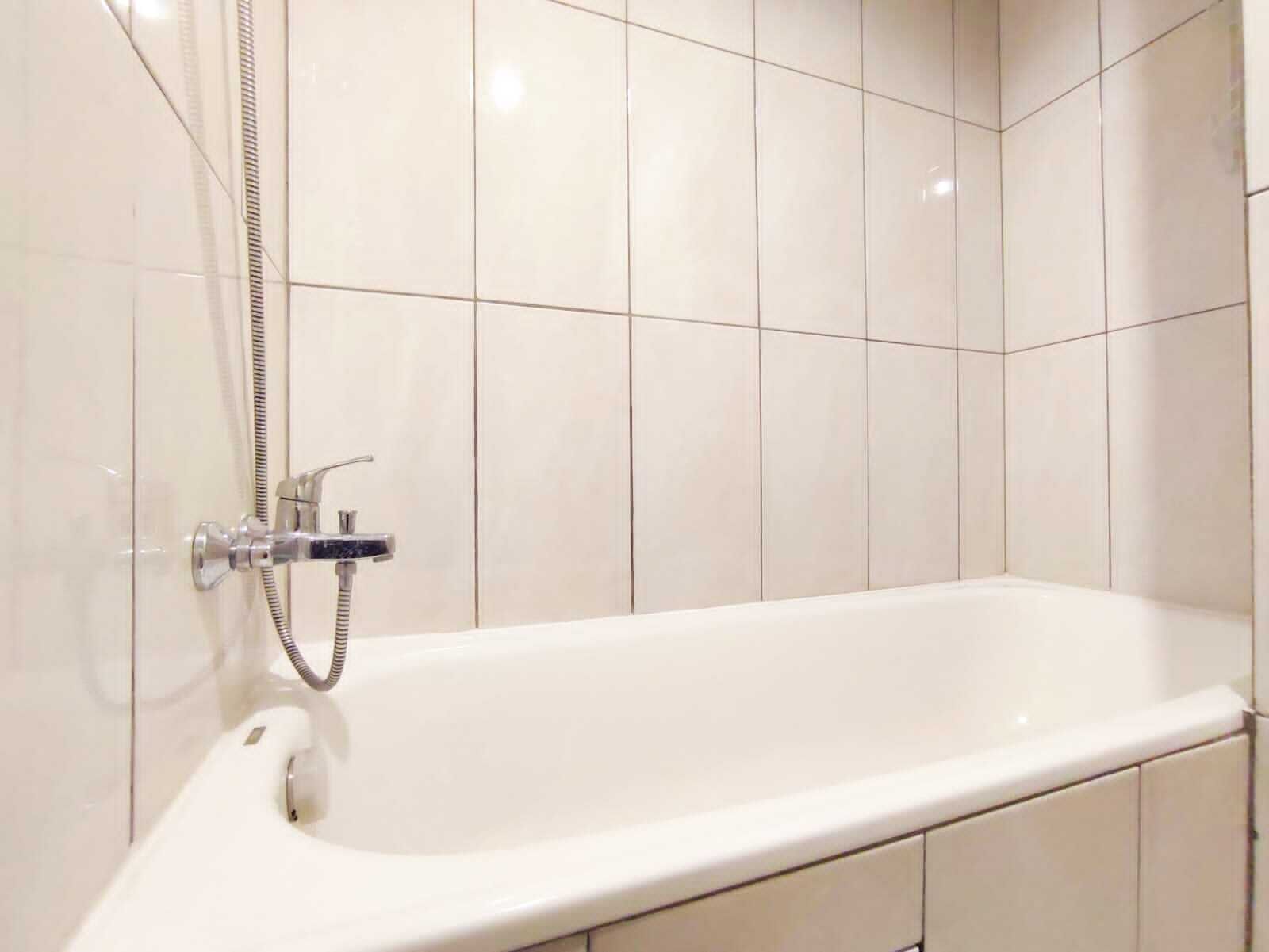 Ein modernes Badezimmer mit einer weißen Badewanne, chromfarbenen Armaturen und weiß gefliesten Wänden.