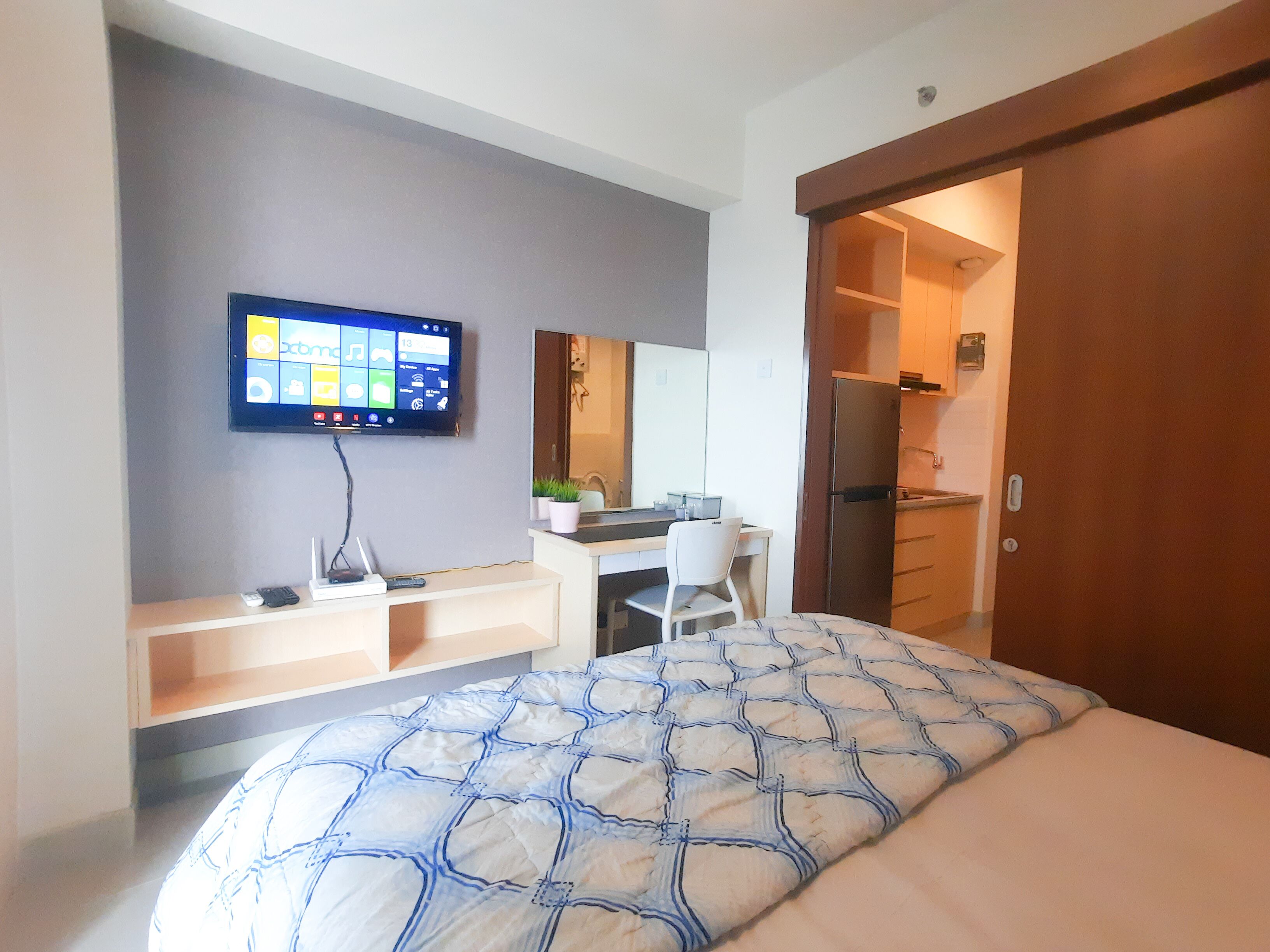 A modern hotel room with a bed, a desk, a chair, a TV mounted on the wall, and a door leading to a bathroom.