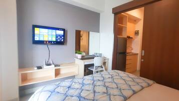 A modern hotel room with a bed, a desk, a chair, a TV mounted on the wall, and a door leading to a bathroom.