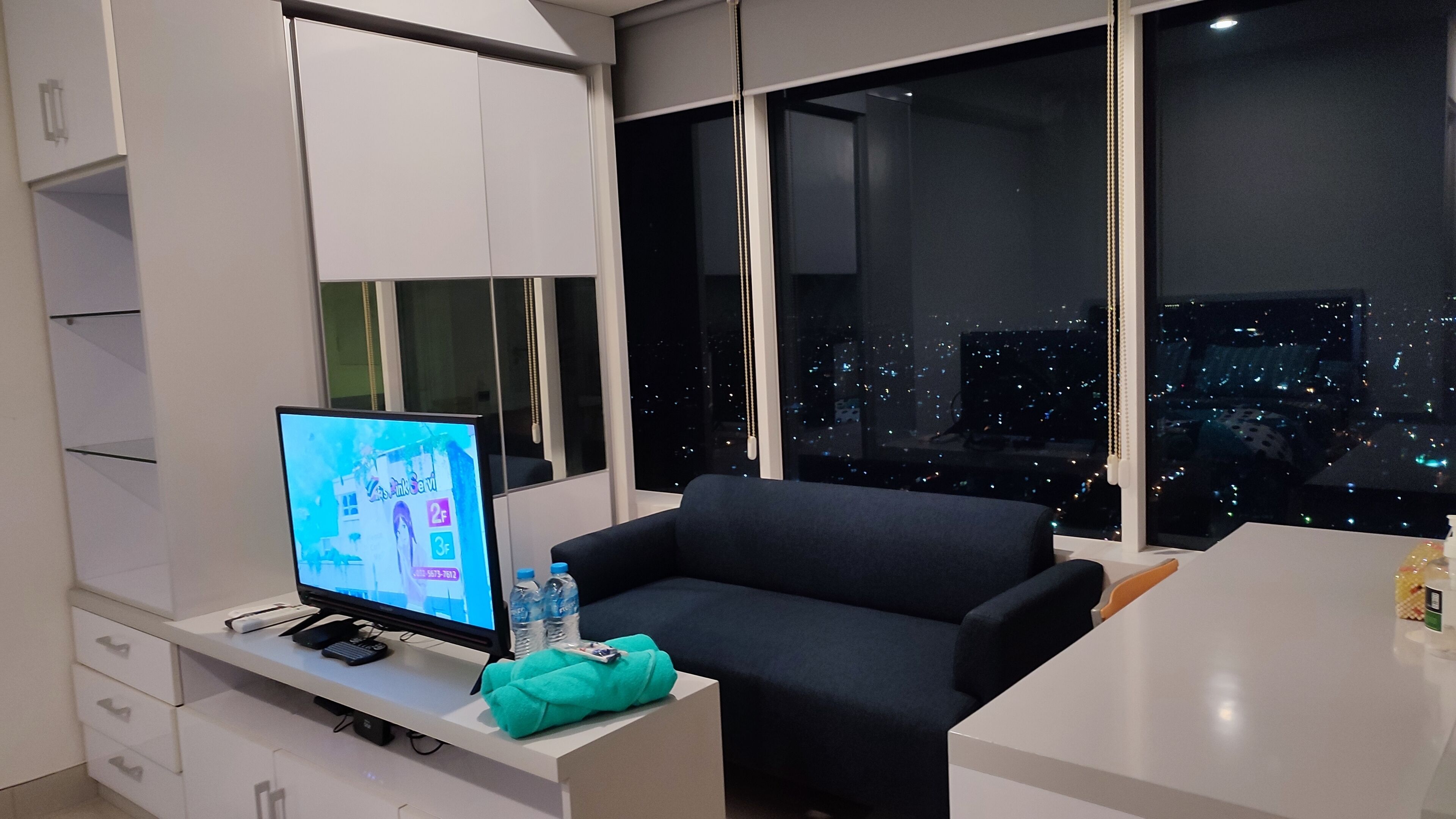 A modern room with a large window, a flat-screen TV, a sofa, and a white desk.