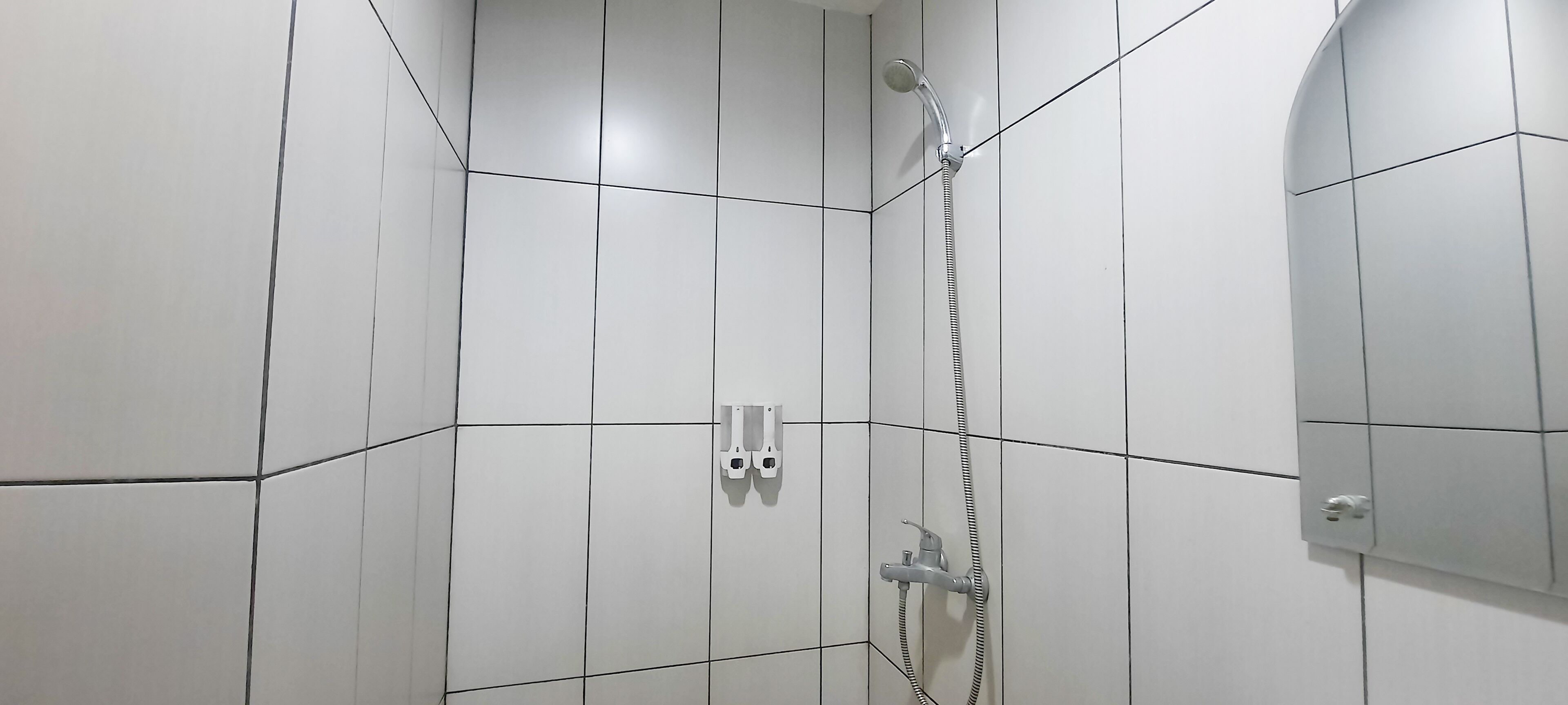 A shower area with white tiled walls and a shower head.