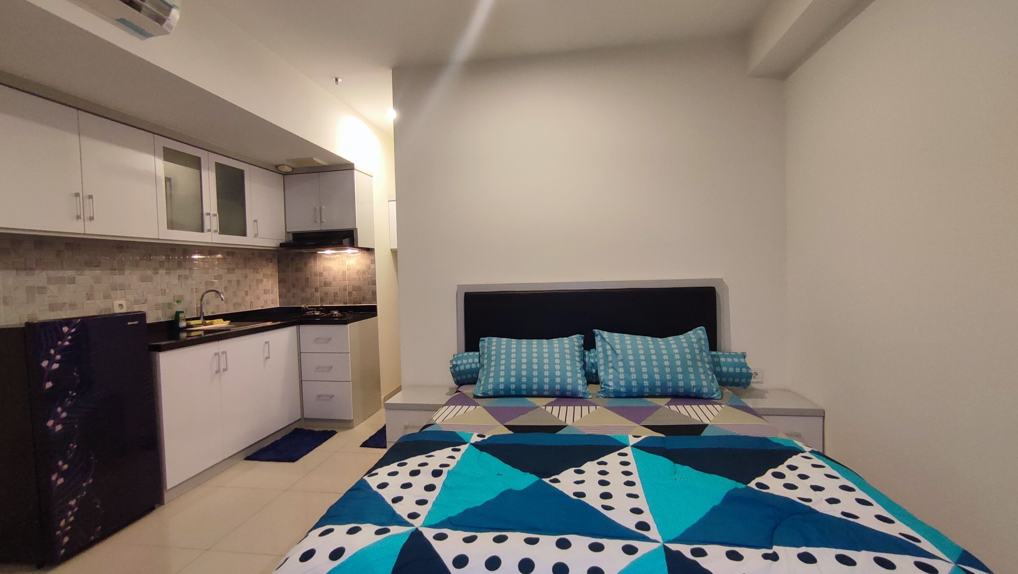 A small, compact bedroom with a bed, a nightstand, and a kitchenette.