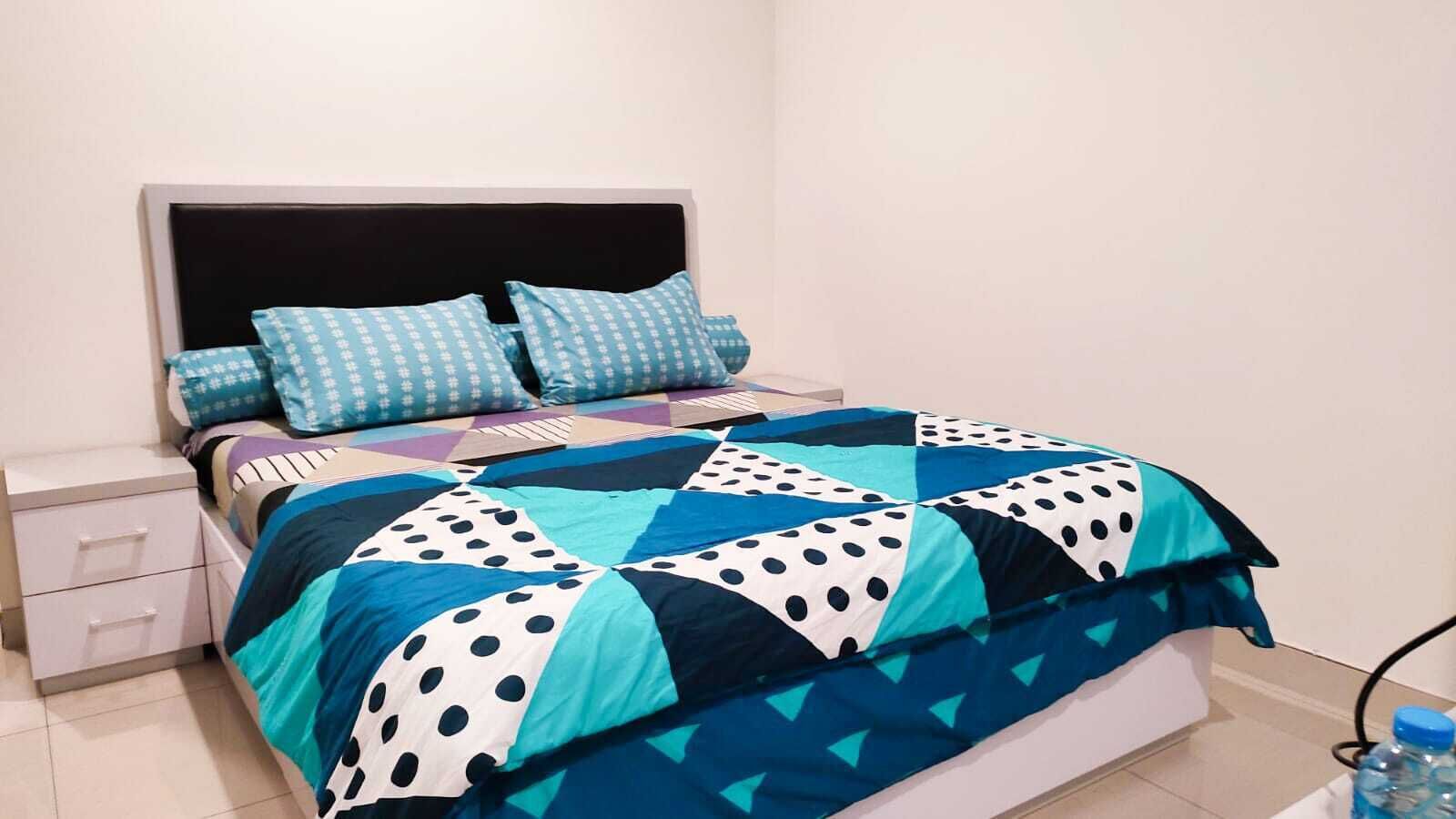 A bed with a blue and white polka dot quilt, a white nightstand with drawers, and a blue water bottle on the floor.