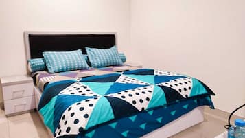 A bed with a blue and white polka dot quilt, a white nightstand with drawers, and a blue water bottle on the floor.