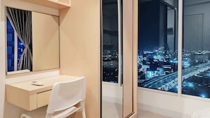A modern bedroom with a large window offering a city view at night. - Grand Kamala Lagoon By Mitra Propertindo (Bekasi)