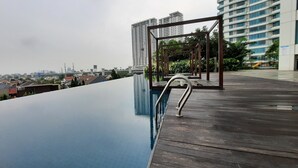A rooftop infinity pool with a wooden deck and metal railings. - Grand Kamala Lagoon By Mitra Propertindo (Bekasi)