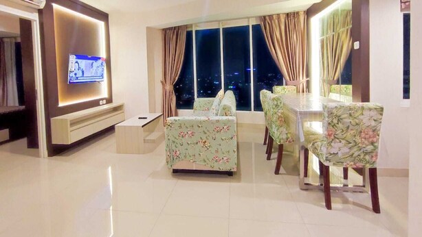 A modern living room with a flat-screen TV, floral-patterned sofa, dining table, and chairs. - Grand Kamala Lagoon By Mitra Propertindo (Bekasi)
