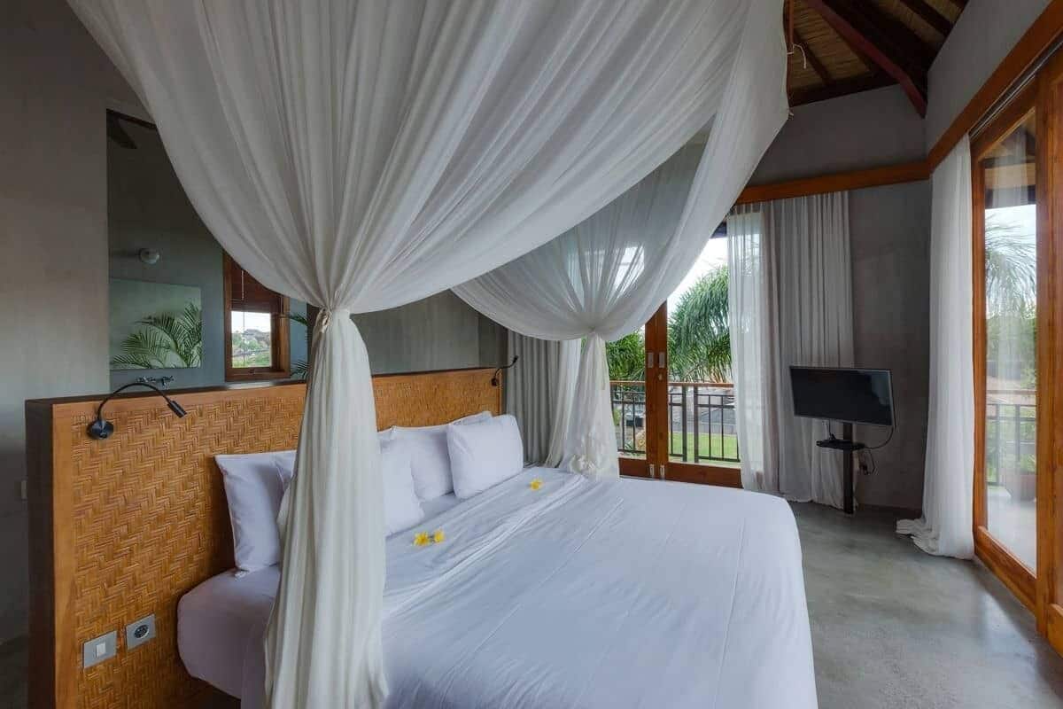 A bedroom with a large bed, white curtains, and a TV in the corner.