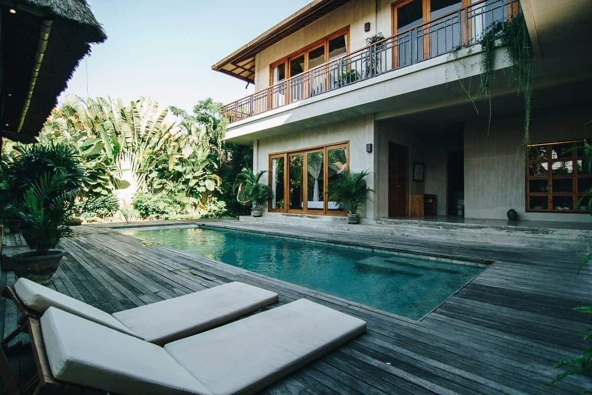 A modern house with a pool, wooden deck, and lush greenery.