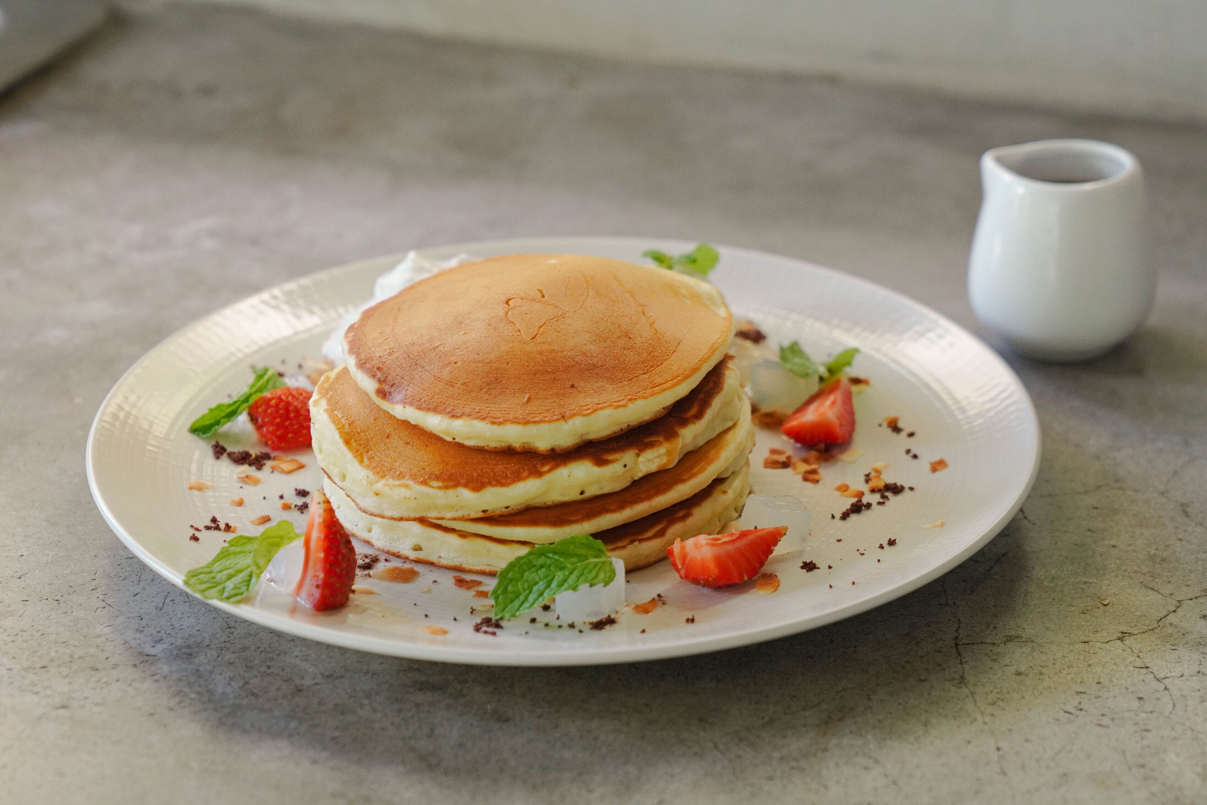 Una pila de tortitas en un plato con fresas y hojas de menta.