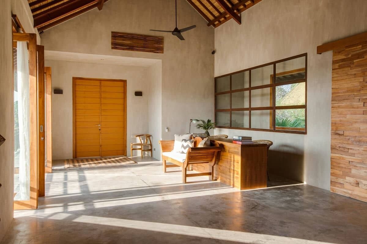 Una habitación amplia con una gran puerta de madera, un mostrador de recepción también de madera y un ventanal con vistas a zonas verdes.