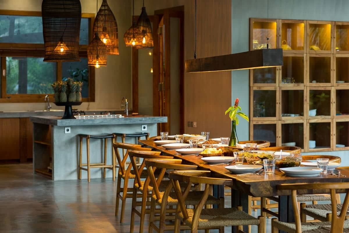 Cocina moderna con una isla central, sillas de madera y lámparas colgantes.