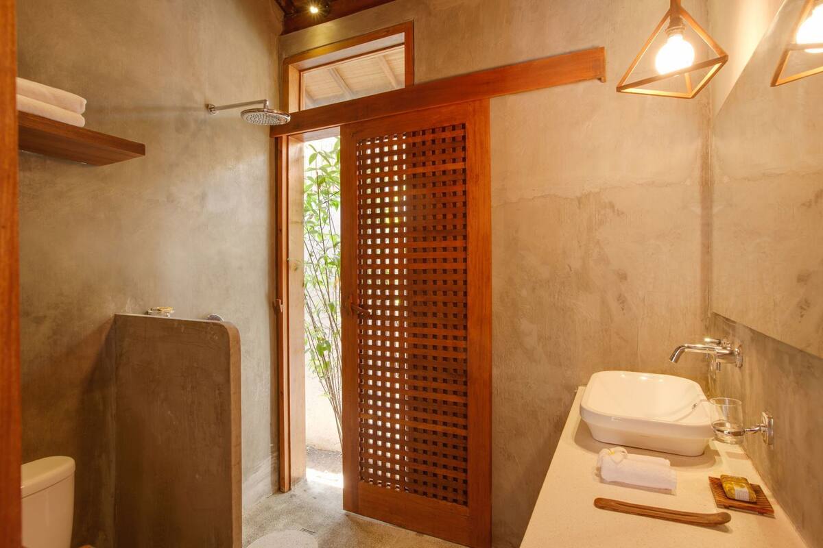 A bathroom with a shower, toilet, sink, and wooden door.