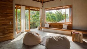 A room with a large window, wooden bench, and bean bag chairs. -  ZIN Berawa Villas & Bungalow (Tibubeneng)