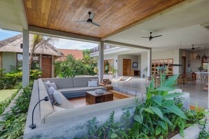 Un amplio espacio exterior con diseño moderno, que incluye un gran sofá, una zona de comedor y una cocina al fondo.