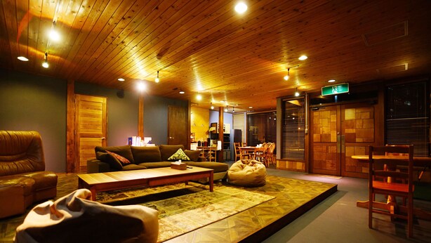 A cozy living room with a wooden ceiling, a sofa, a coffee table, and a bean bag. - HAKUBA Lodge OMUSUBI (Otari)