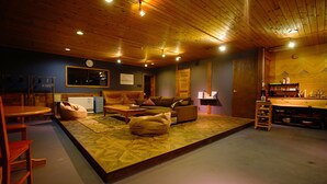 A cozy living area with a sofa, chairs, a coffee table, and a kitchen area in the background. - HAKUBA Lodge OMUSUBI (Otari)